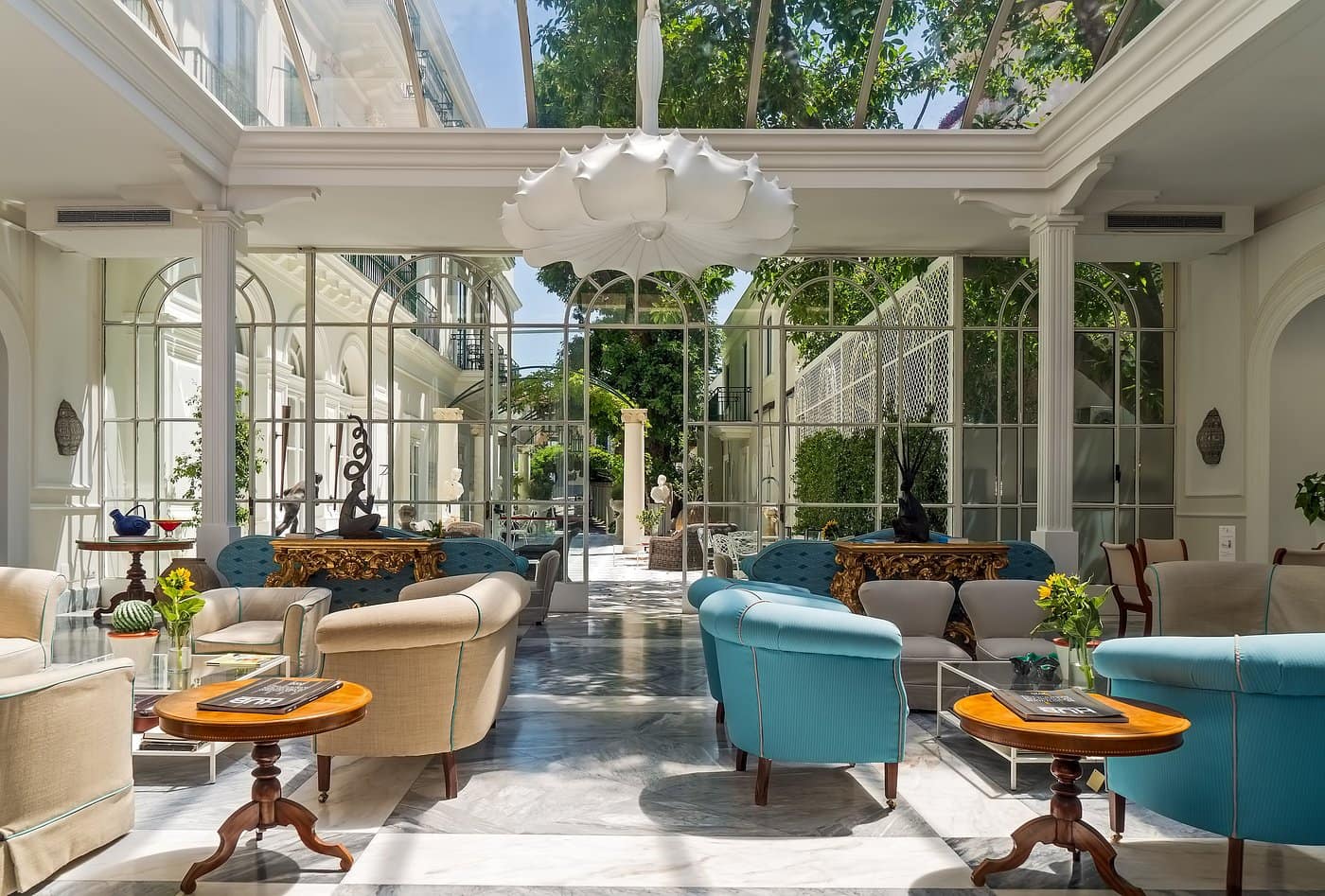 Veranda vetrata del Bellevue Syrene, con divani turchesi e affaccio sul giardino interno