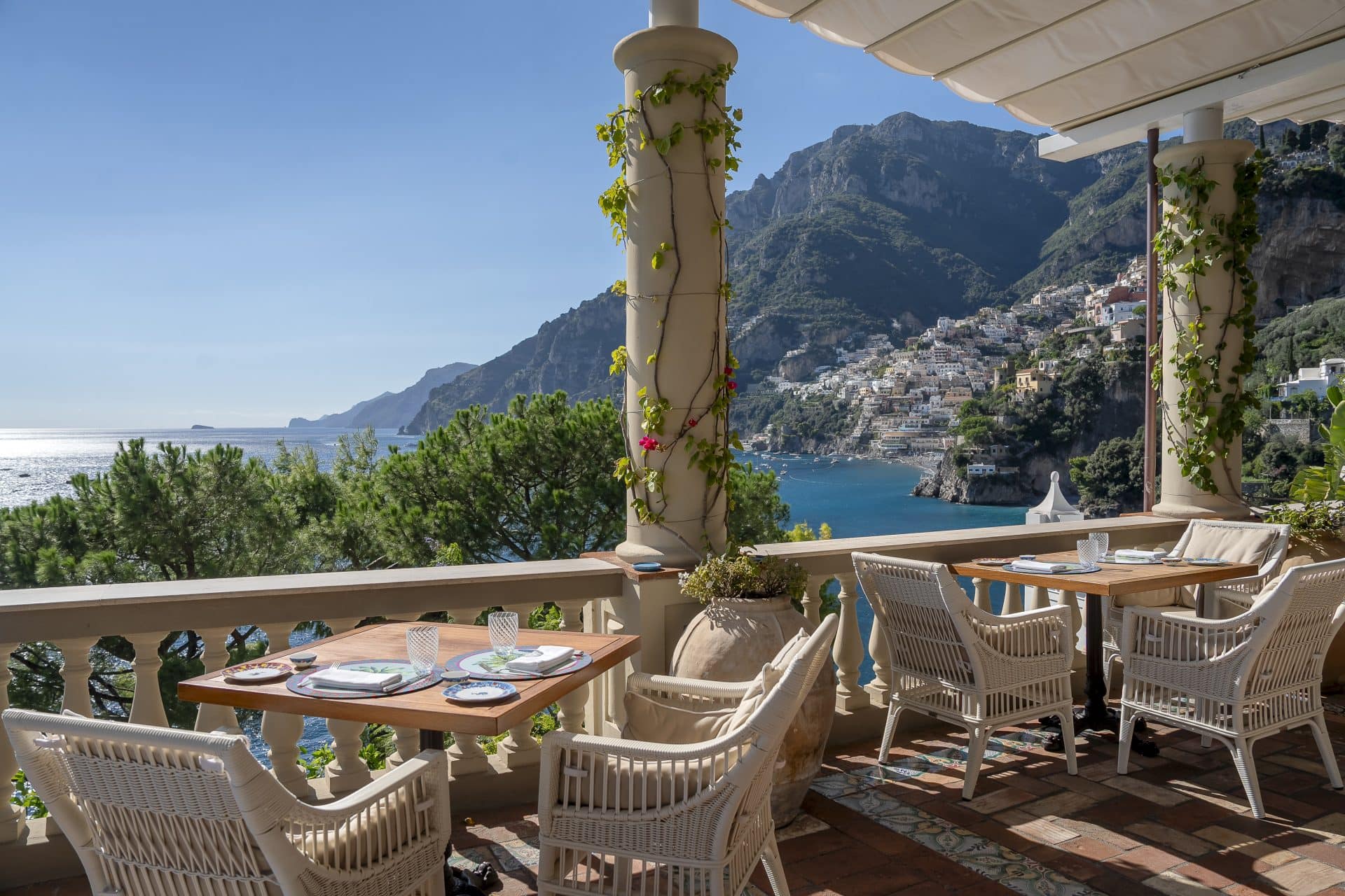 Terrazza coperta di Villa TreVille con tavoli apparecchiati e colonne coperte di bougainvillea, affacciata sul mare e sul borgo di Positano